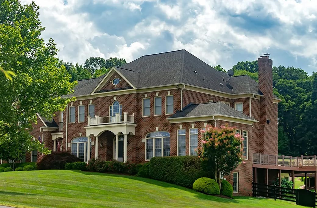Elegant brick mansion with manicured lawn and lush trees, reminiscent of Greenbrier Farm.