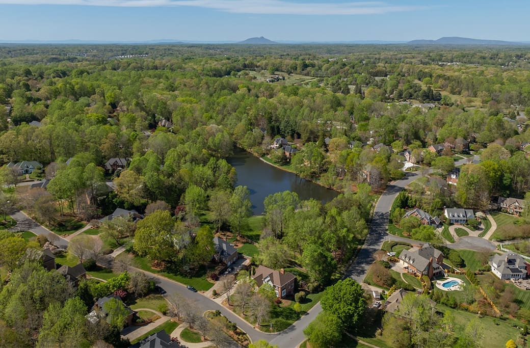 Aerial view of Greenbrier Farm homes nestled among lush trees surrounding a serene pond.