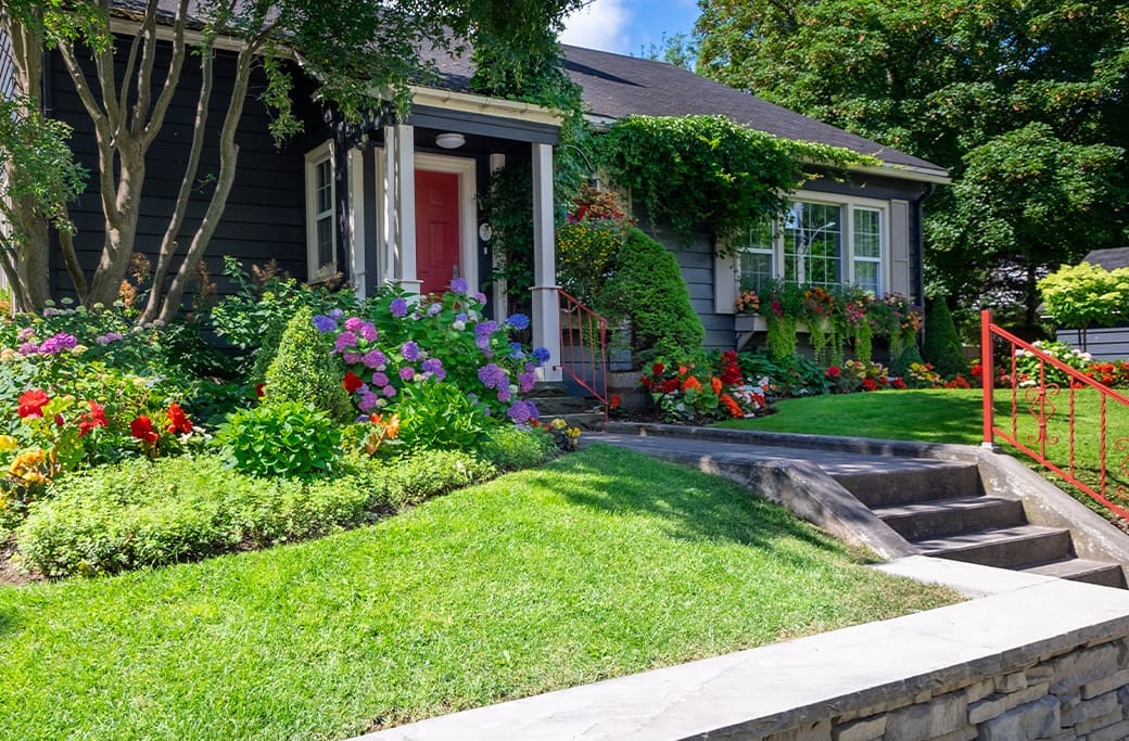 Charming dark gray house with a vibrant red door and abundant colorful flowers, ideal for home staging.