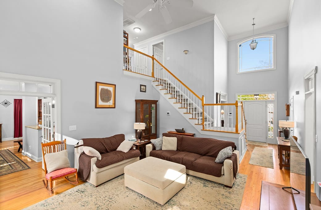 Spacious living room with high ceilings, staircase, and elegant furniture, ready for home buyers.